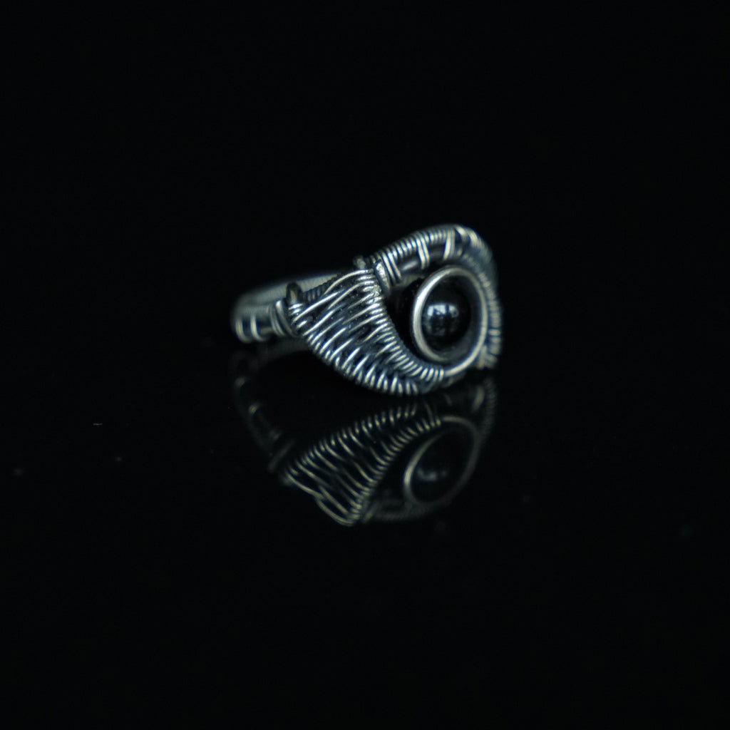 Three-quarter view of The Eclipse natural black obsidian ring showing its hand-shaped brass
wirework
