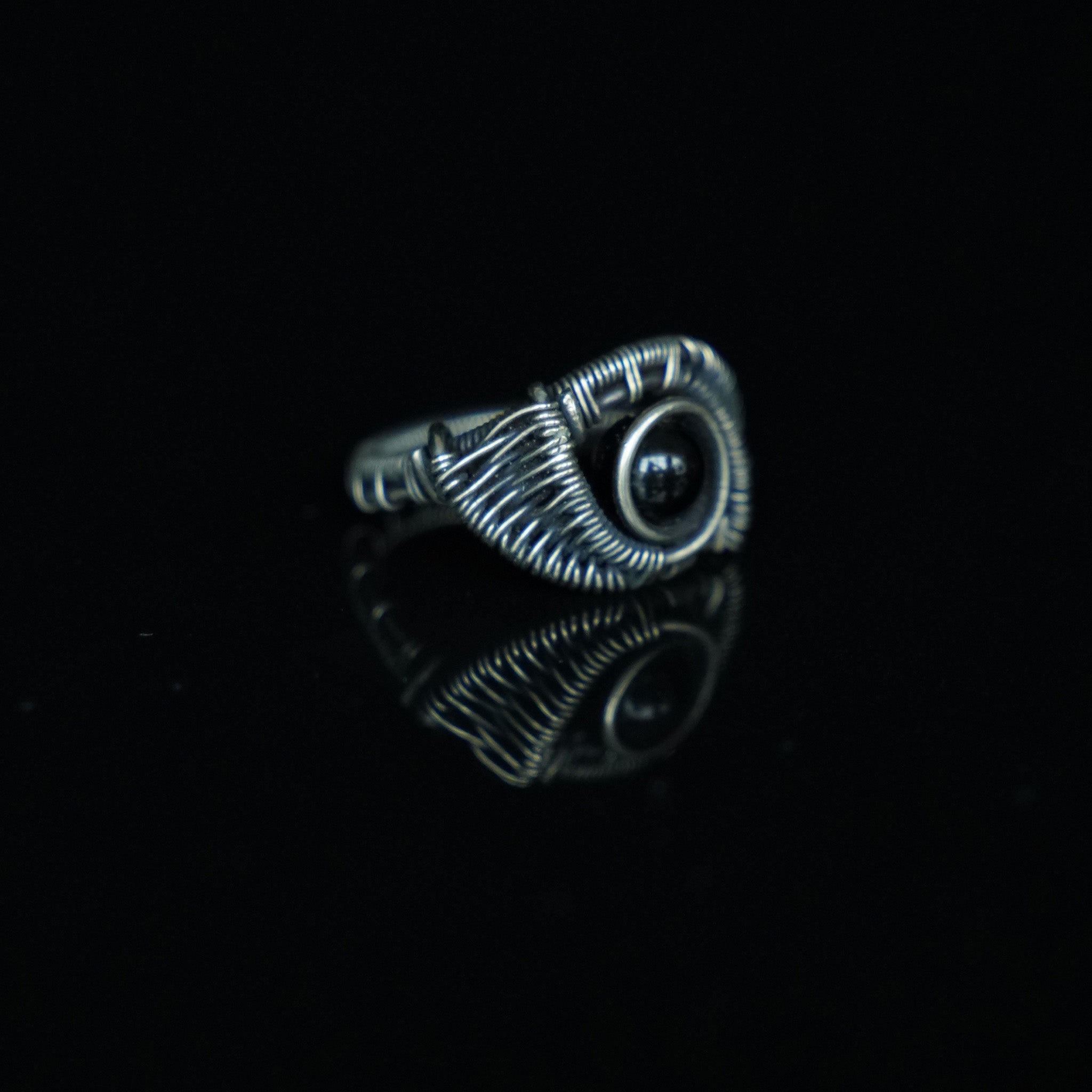 Three-quarter view of The Eclipse natural black obsidian ring showing its hand-shaped brass
wirework