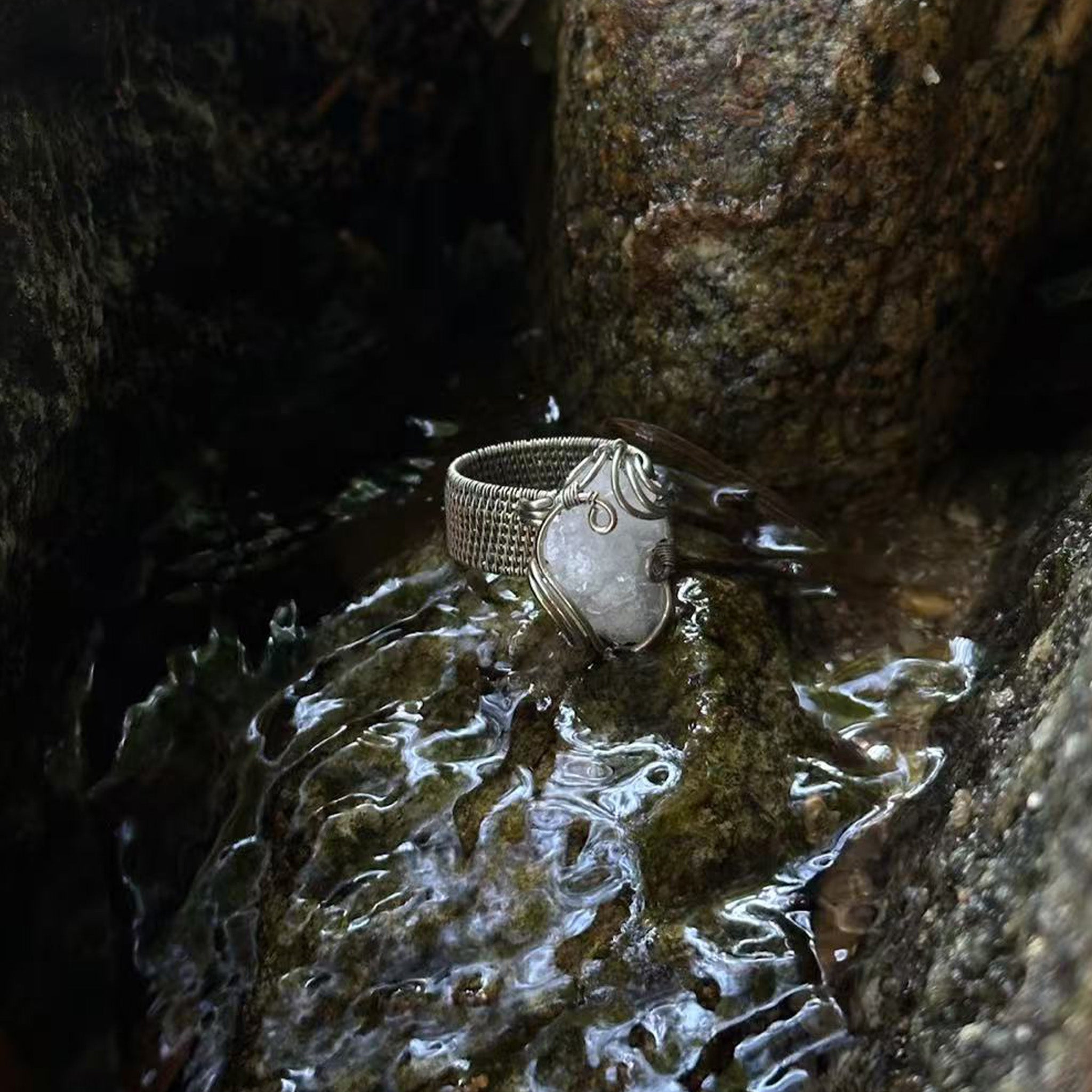 The Quiet Frost natural crystal cluster ring with white copper wirework resting on wet rocks
outdoors