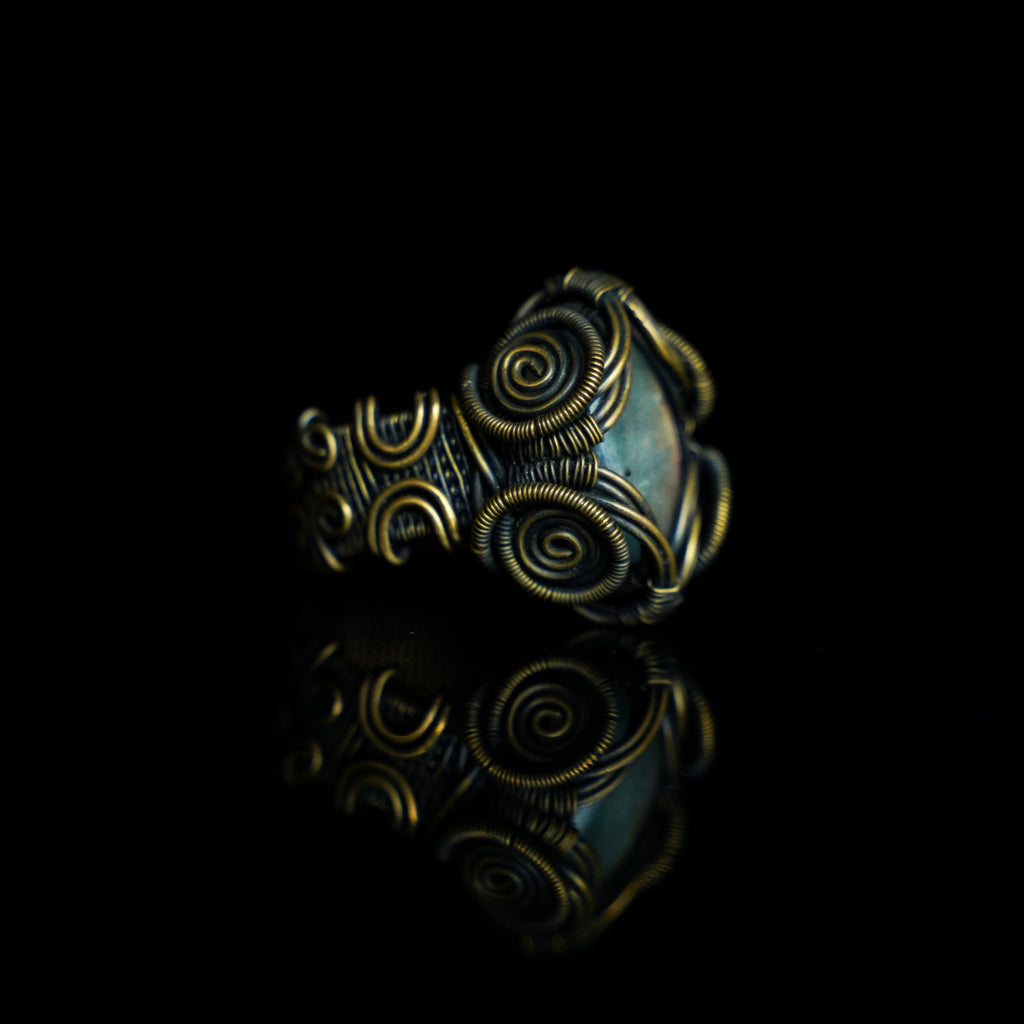 Three-quarter view of The Veil natural labradorite ring with hand-shaped brass wirework
